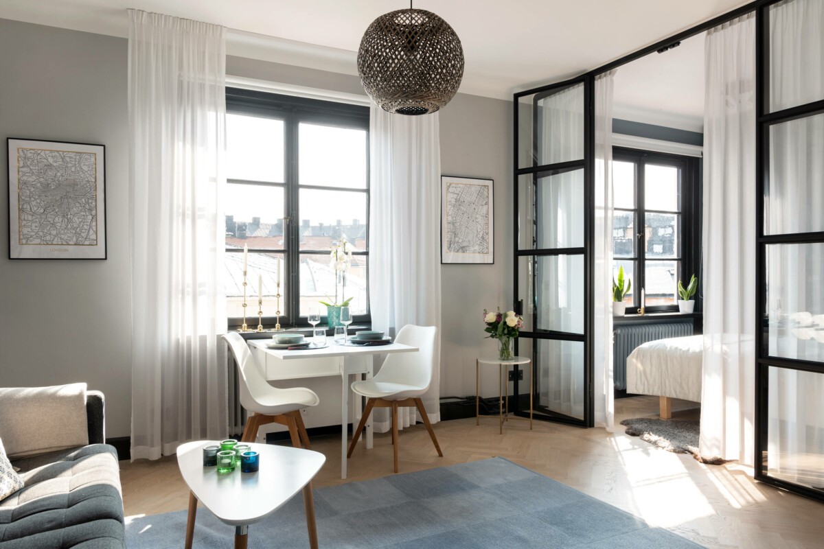 vivienda para una persona toques de azul pocos muebles planta abierta mobiliario ligero marcos negros funcionalidad estilo nórdico dormitorio con pared de cristal decoración escandinava decoración compacta colores neutros cocina gris topo cocina en U apartamento pequeño 