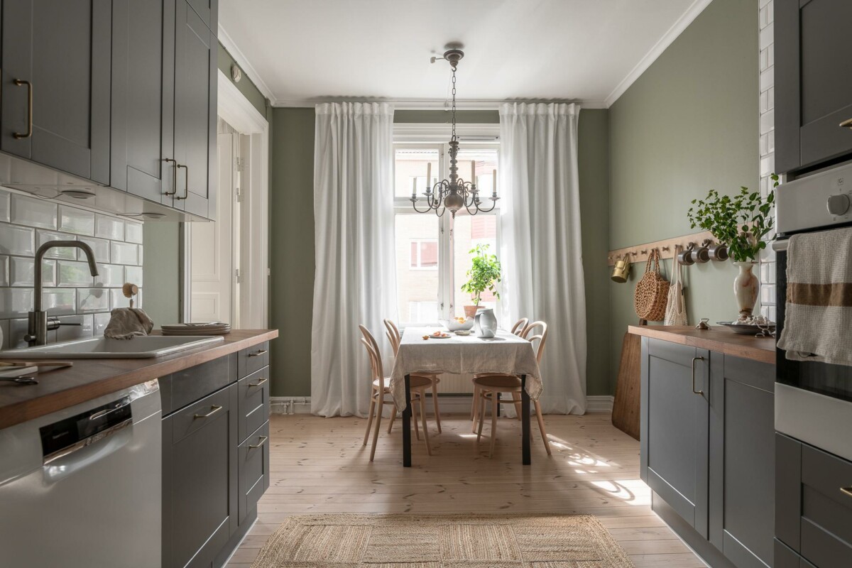 wooden countertop vivienda de segunda mano second-hand home scandinavian kitchen pantry muebles cocina verdes large window lámpara de araña green kitchen furniture gran ventanal encimera de madera Elegante cocina nórdica verde elegant green Nordic kitchen despensa curtains cortinas cocina escandinava cocina cerrada closed kitchen chandelier 